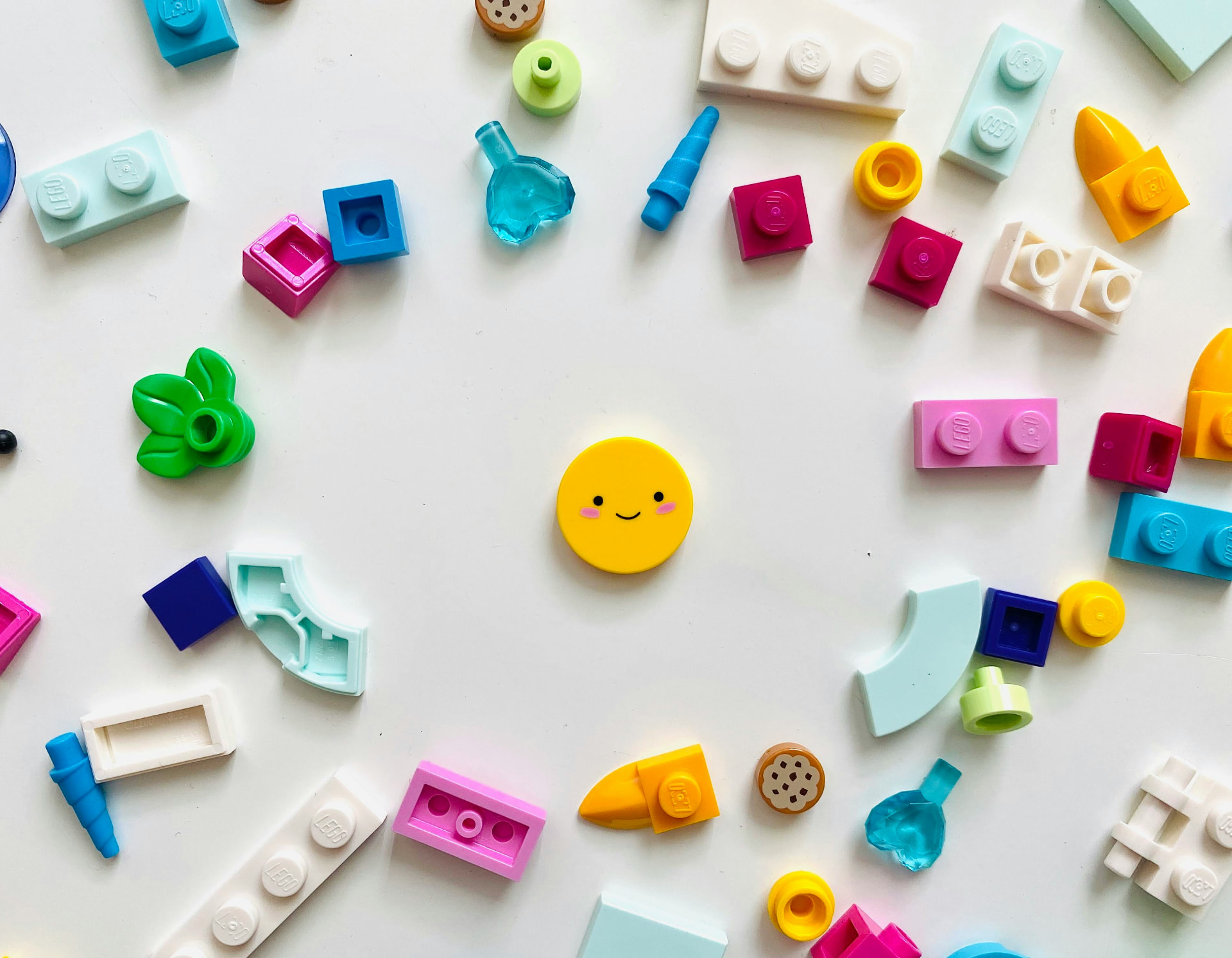 Colorful LEGO pieces and small toy parts scattered on a clean white background